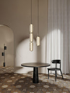 Two Clérachic ribbed glass pendants, a stacked one and a single, hang above a round table and black chair, beside a pale curtain.