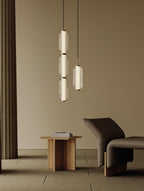 A stacked and a single ribbed glass Clérachic pendant glow in a beige room with a wooden side table and a dark lounge chair.
