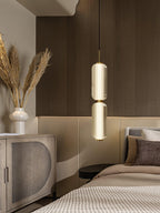 A two-tier ribbed glass Clérachic pendant glowing at a bedside, with dried grasses, a cream vase and a rattan cabinet.