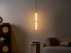 A two-tier Clérachic ribbed glass pendant glows warmly against a dark wall, with a rattan cabinet and a sofa in shadow.