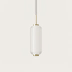 A ribbed clear glass Clérachic pendant with a gold stem, hanging on a plain warm-white backdrop.