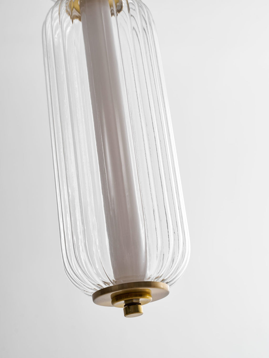 Close view of the lower tip of a ribbed clear glass Clérachic pendant, with its white inner tube and gold cap.
