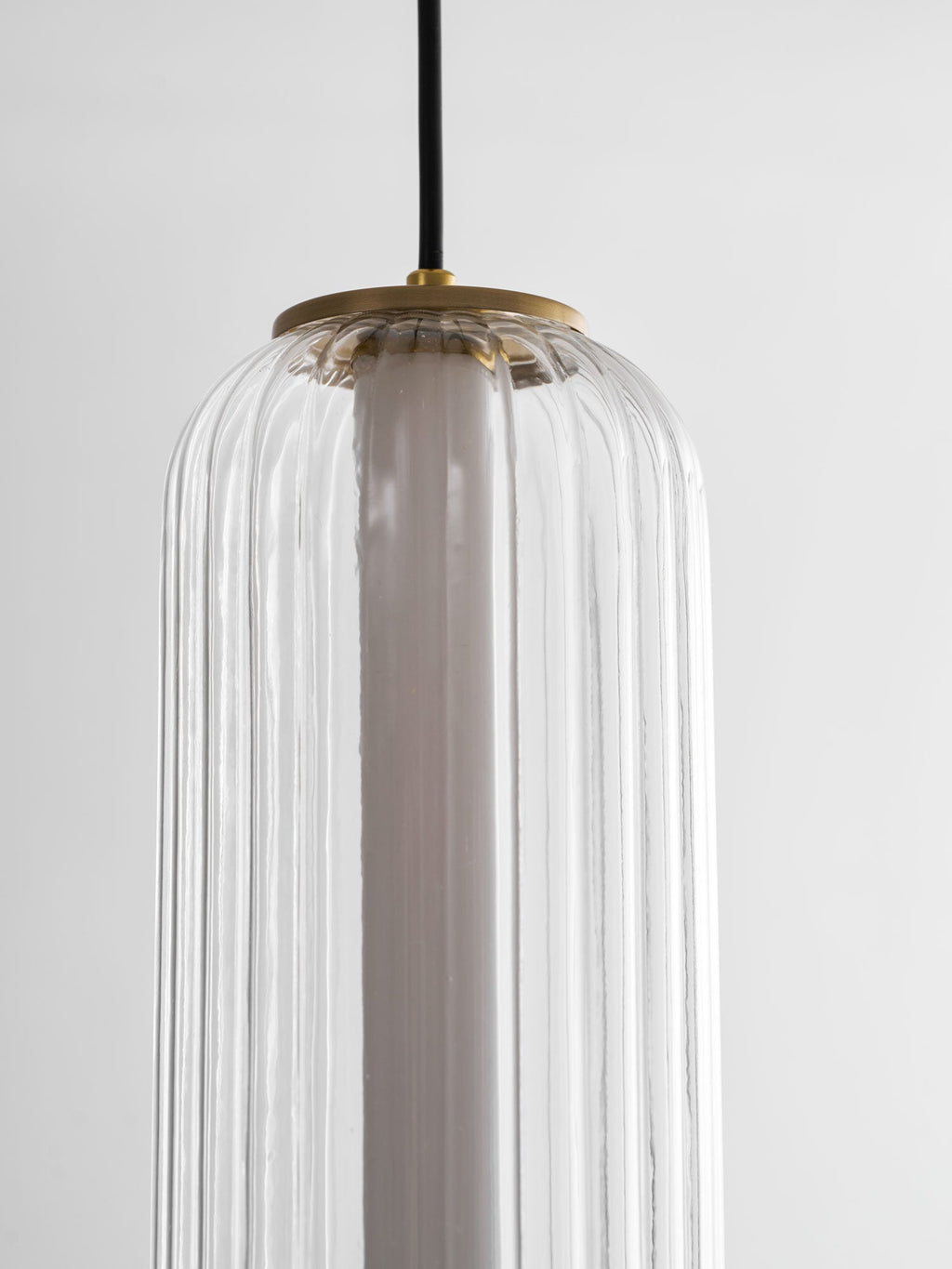 Close view of the top of a ribbed clear glass Clérachic pendant, showing the gold canopy cap and white inner tube.