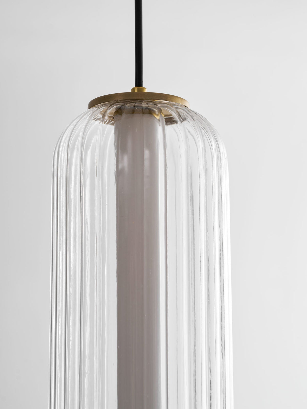 Close view of the top of a ribbed clear glass Clérachic pendant, showing the gold canopy cap and white inner tube.