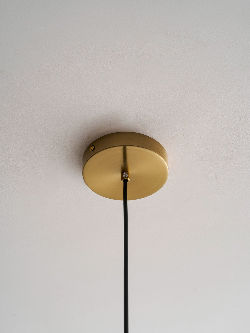 Close view of the round gold ceiling canopy on a Clérachic pendant, with its black cord leaving the centre.