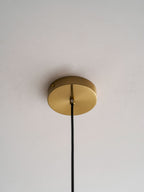 Close view of the round gold ceiling canopy on a Clérachic pendant, with its black cord leaving the centre.