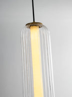 Close view of the lit upper tier of a ribbed clear glass Clérachic pendant, with a glowing white inner tube and gold cap.