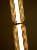 Close view of the gold collar between two lit, ribbed glass tiers of a Clérachic pendant, against a dark background.