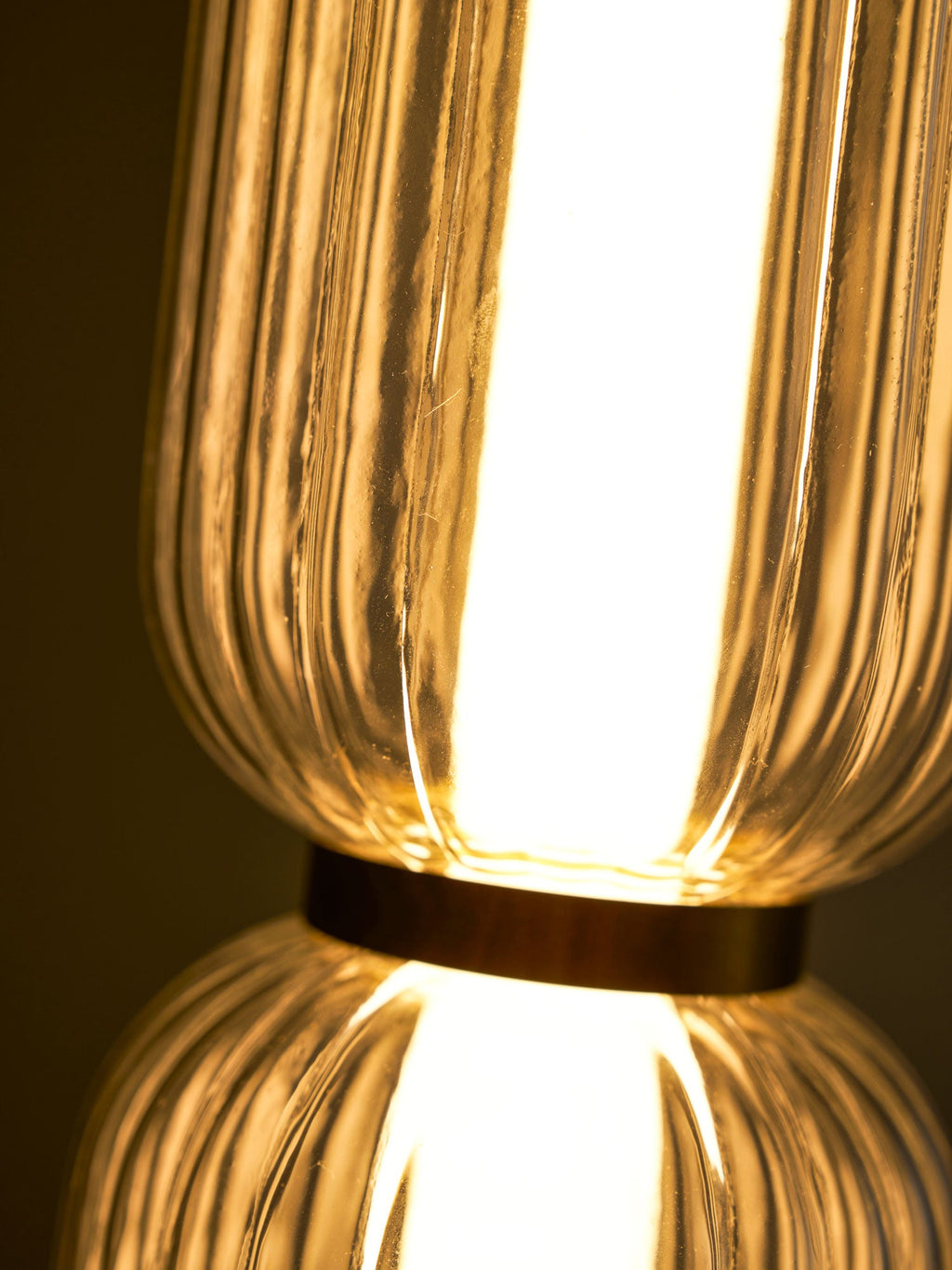 Close view of the gold band joining two glowing ribbed glass tiers on a Clérachic pendant, with fine glass ridges.