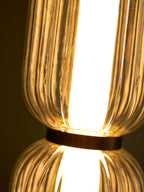 Close view of the gold band joining two glowing ribbed glass tiers on a Clérachic pendant, with fine glass ridges.