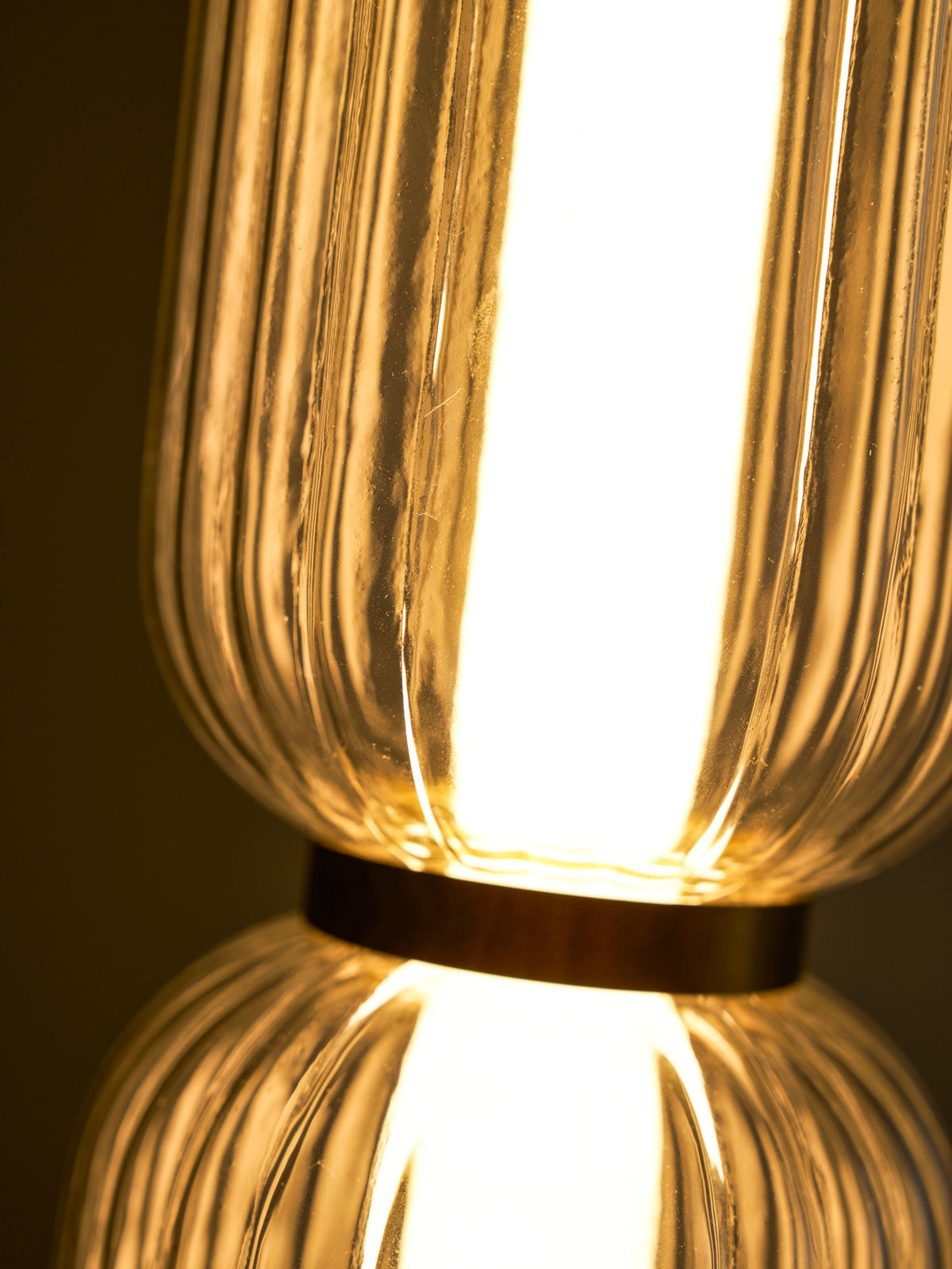 Close view of the gold band joining two glowing ribbed glass tiers on a Clérachic pendant, with fine glass ridges.