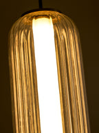 Close view of the top of a ribbed glass Clérachic pendant glowing warm, with the white light tube visible inside.