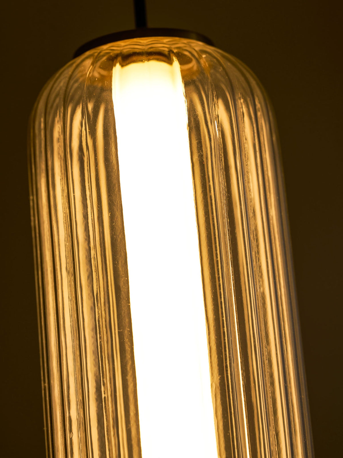 Close view of the top of a ribbed glass Clérachic pendant glowing warm, with the white light tube visible inside.