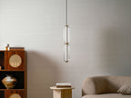 A two-tier ribbed clear glass Clérachic pendant, unlit, above a rattan cabinet and a stone side table in a pale room.