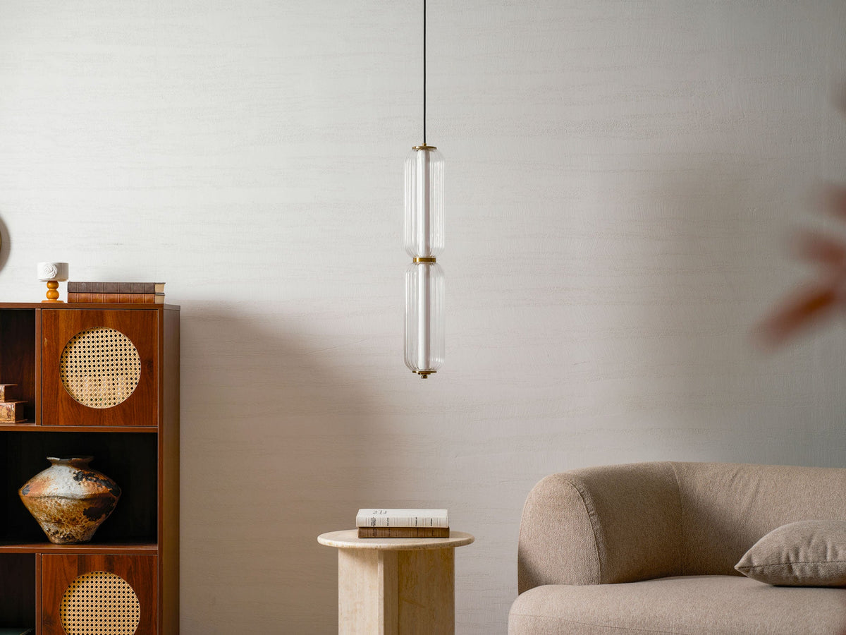 A two-tier ribbed clear glass Clérachic pendant hangs before a marble-effect wall, with a rattan cabinet and a stone table.