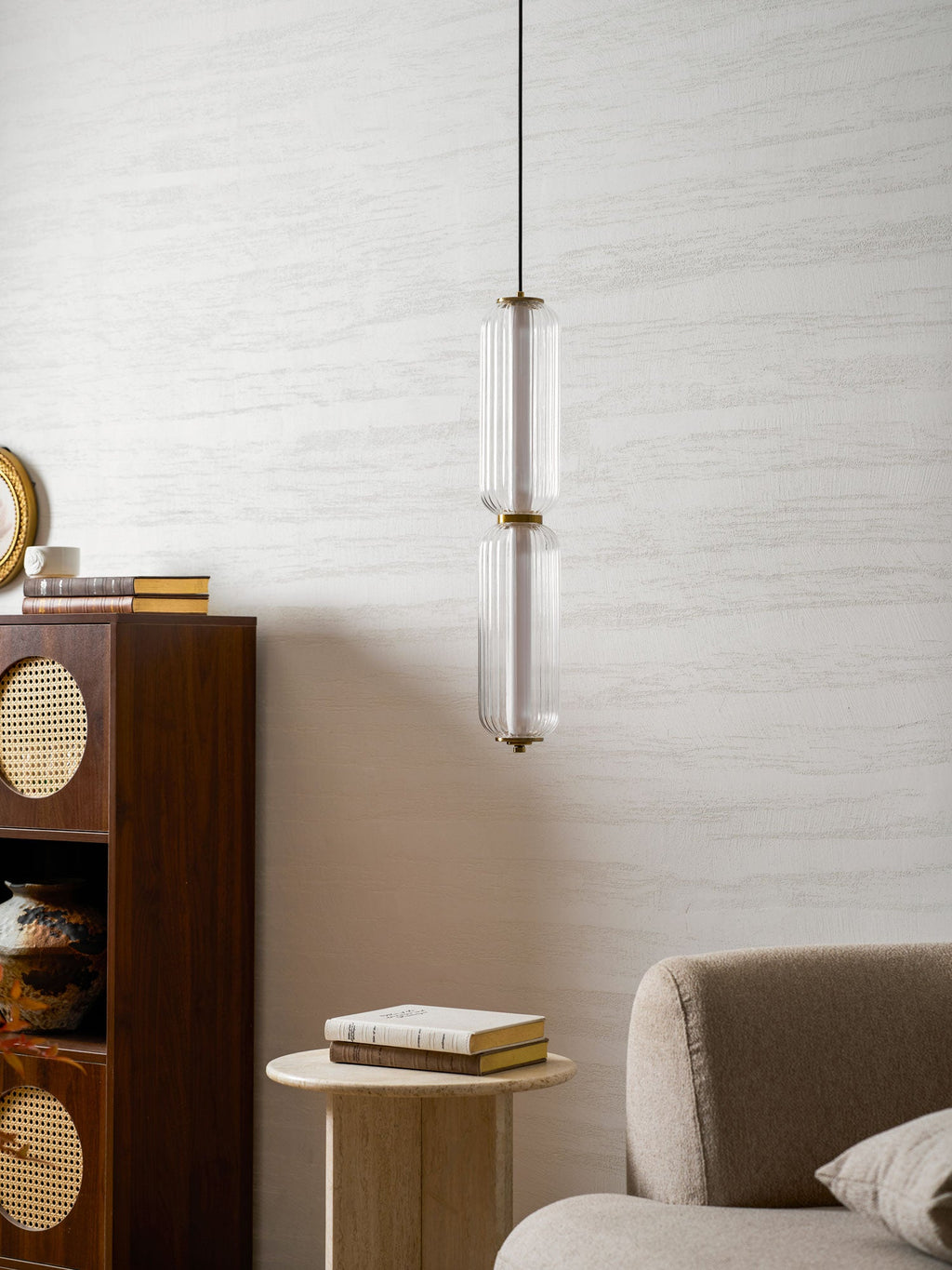 A two-tier ribbed clear glass Clérachic pendant seen closer, before a pale wall, with a rattan cabinet and a boucle sofa.
