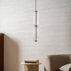 A tall, narrow Clérachic ribbed glass pendant, unlit, close to a pale wall with a stone table and books below.