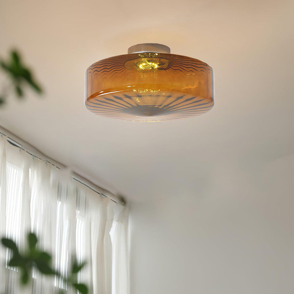 Warm light from the Clérachic Sunburst Amber Glass Flush Mount Ceiling Light spilling across a bedroom ceiling beside sheer white curtains.