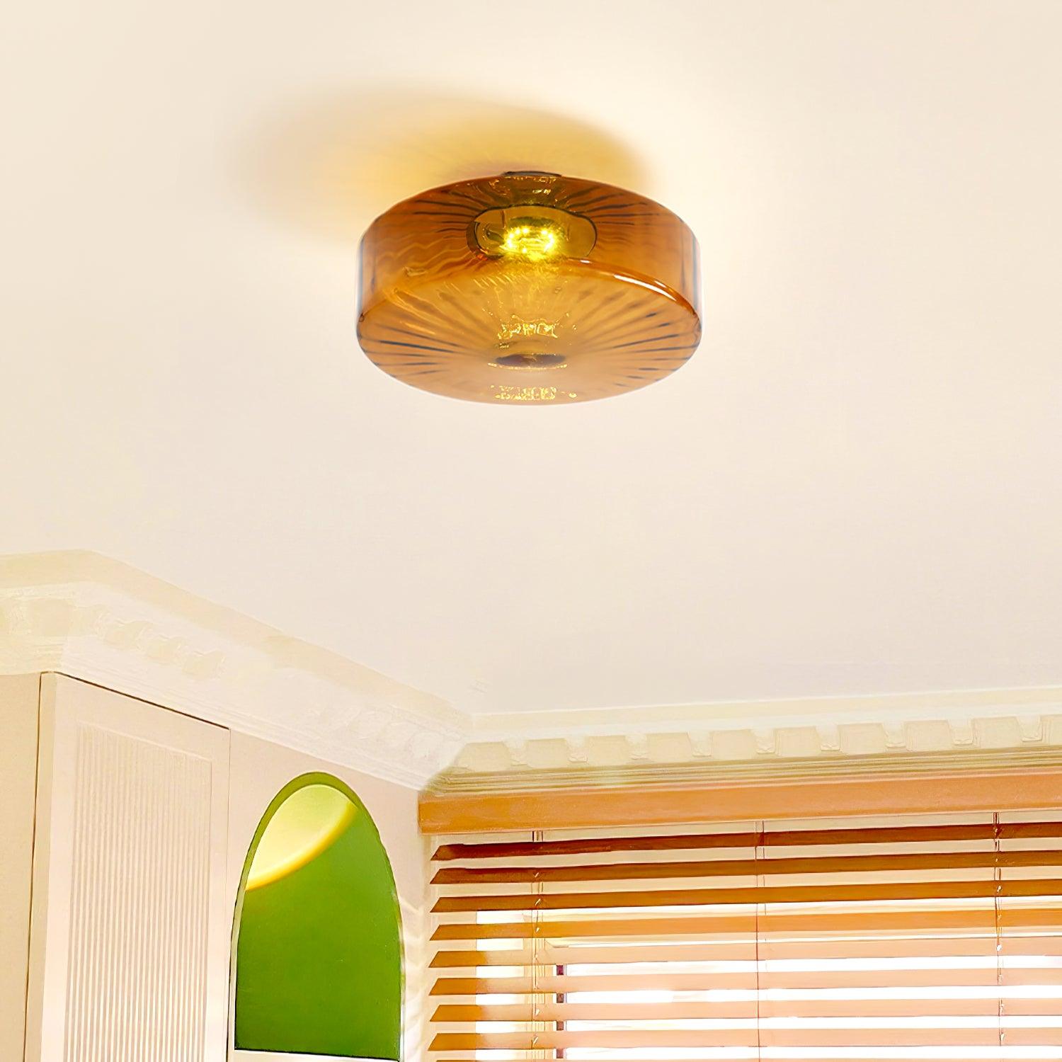 Clérachic Sunburst Amber Glass Flush Mount Ceiling Light lit in a room with wooden venetian blinds and a green arched mirror below.