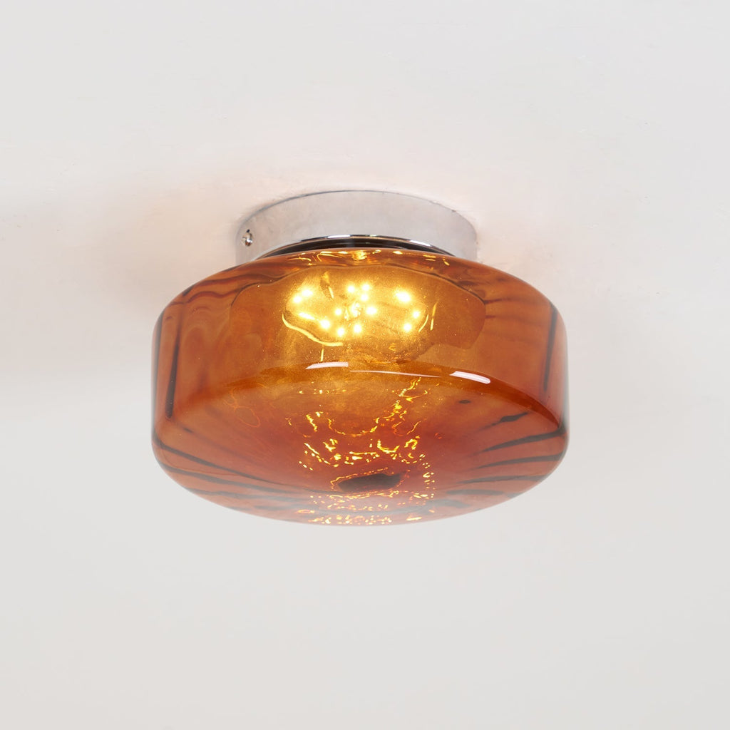 Clérachic Sunburst Amber Glass Flush Mount Ceiling Light lit on a white ceiling, the polished chrome canopy visible above the amber drum.