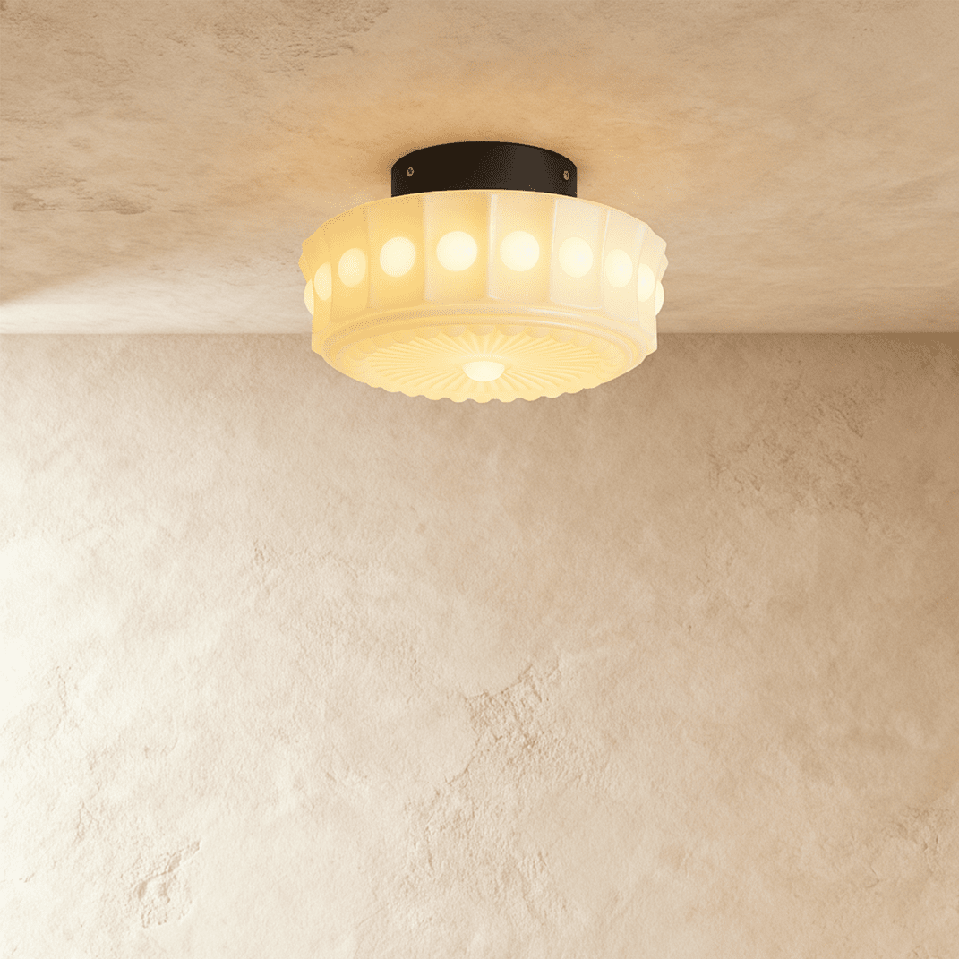 Clérachic flush-mount glass shade glowing warm, round bead windows around the fluted rim, black ceiling plate, limewash wall.