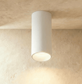 Clérachic surface downlight in white aluminium mounted on a plaster ceiling, casting warm light down a corner wall.