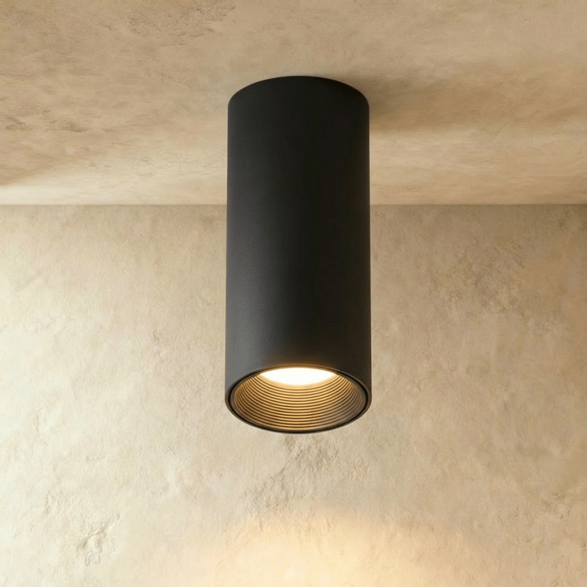 Clérachic surface downlight in matte black aluminium fixed to a plaster ceiling, its warm beam lighting the wall below.