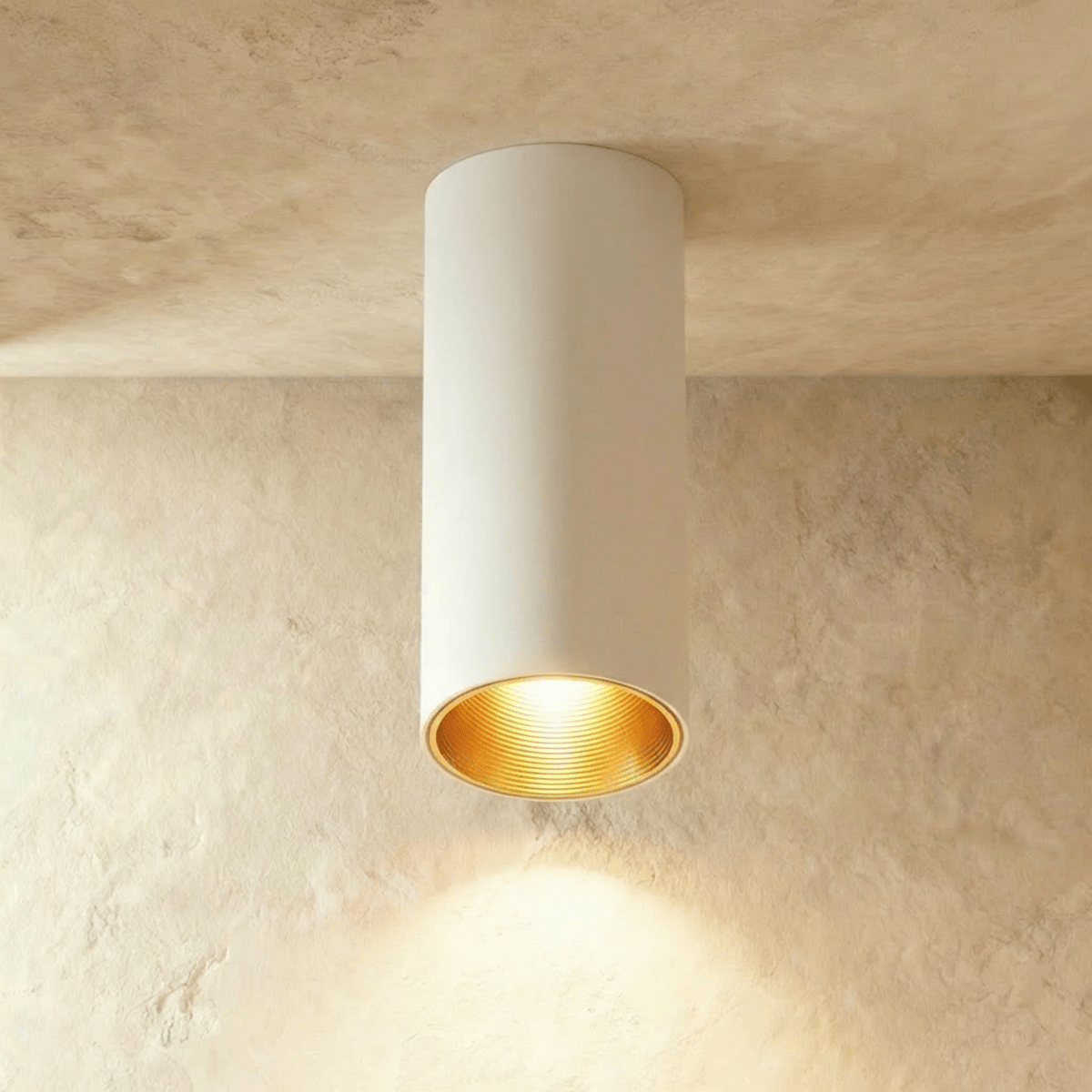 Clérachic surface downlight in white aluminium with a gold-tone baffle, lit warm against a textured plaster ceiling.