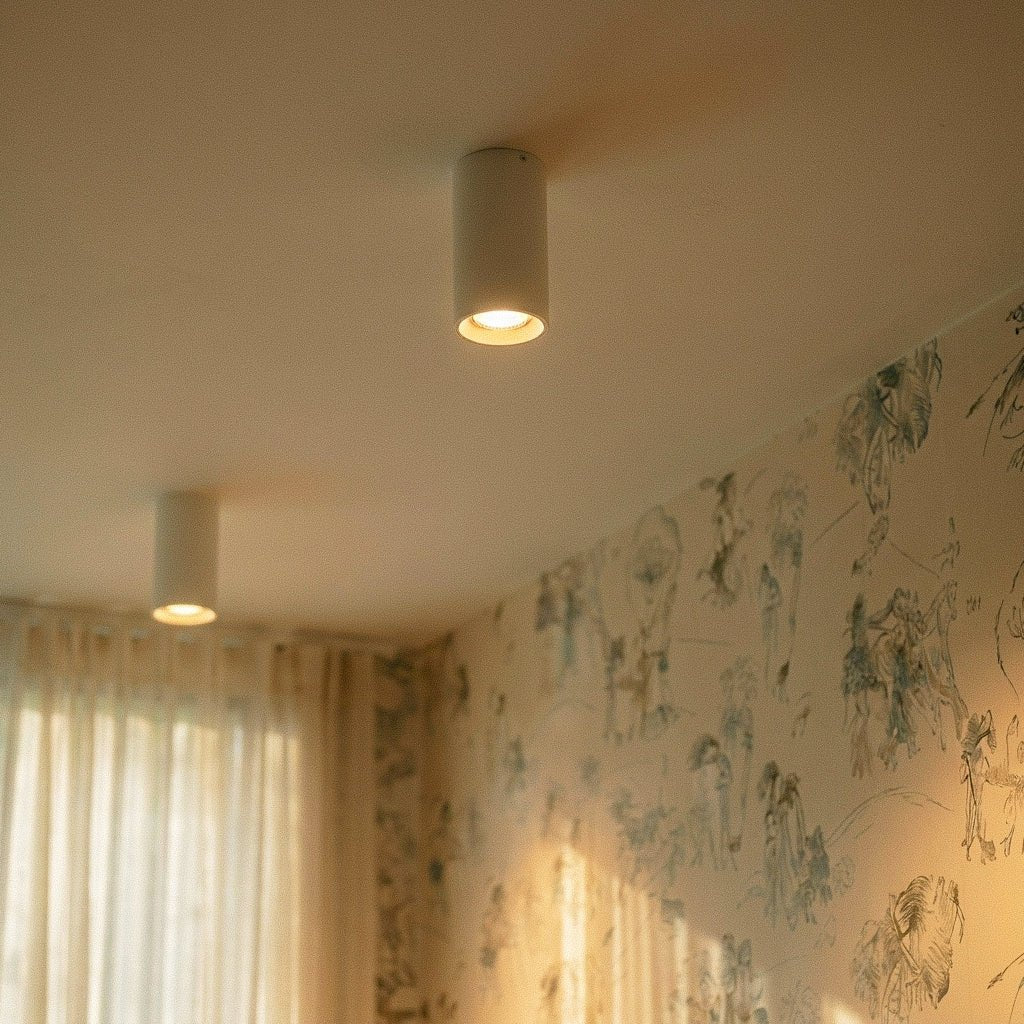 Clérachic surface downlight glows warm on a plaster ceiling above sheer curtains in a softly lit corner room.