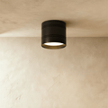 Clérachic compact black surface-mounted downlight with two fine grooves, lit warm white against a limewashed ceiling and wall.