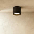 Clérachic compact black surface-mounted downlight with two fine grooves, lit warm white against a limewashed ceiling and wall.
