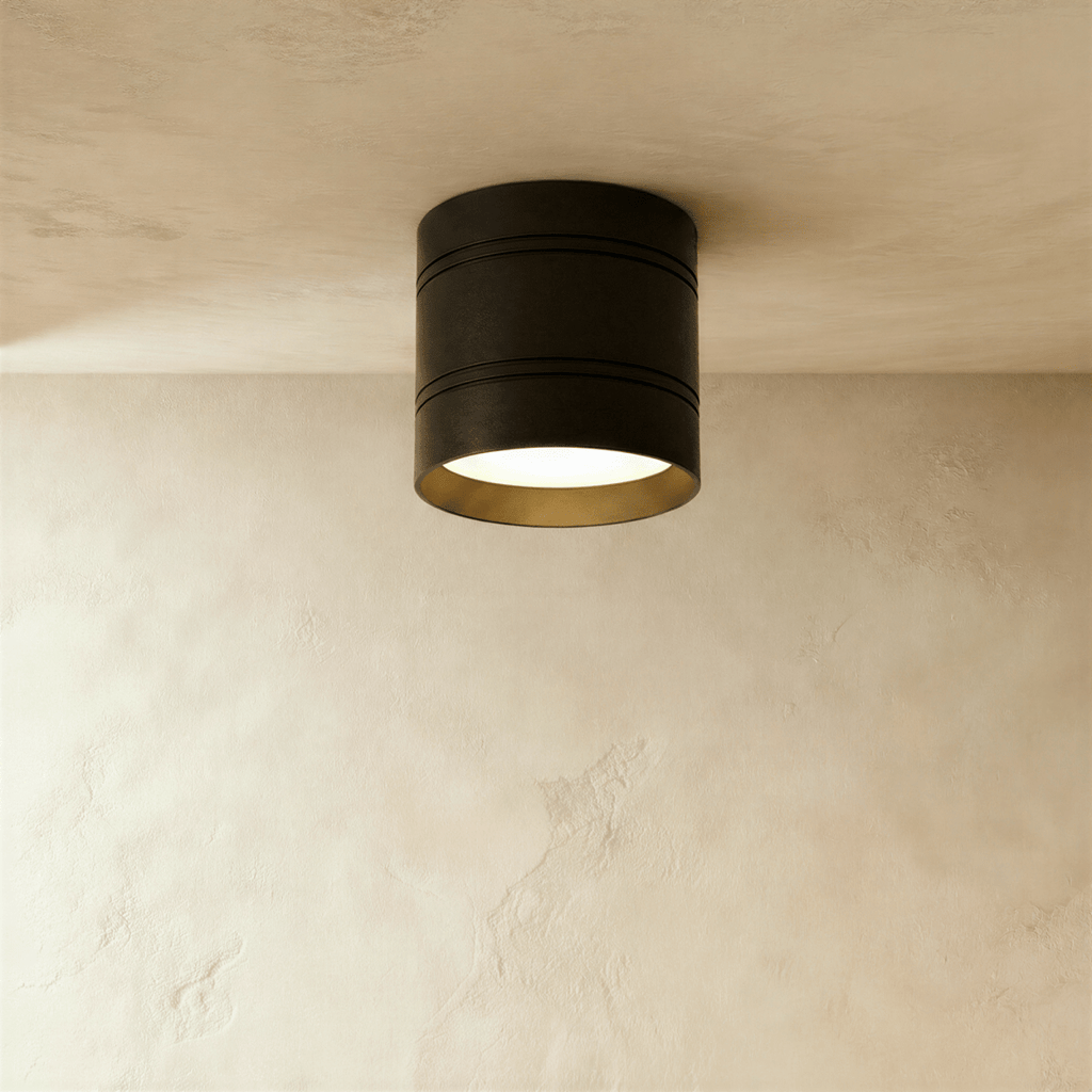 Clérachic larger black surface-mounted downlight with two fine grooves and a gold-toned inner rim, lit on a plaster ceiling.