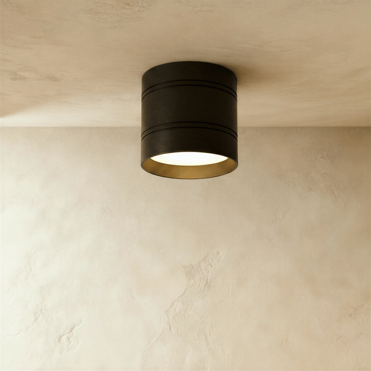 Clérachic larger black surface-mounted downlight with two fine grooves and a gold-toned inner rim, lit on a plaster ceiling.