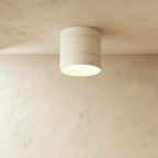 Clérachic larger white cylindrical downlight with two fine grooves, lit softly against a limewashed plaster ceiling.
