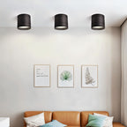 Clérachic row of three black surface-mounted downlights above a living room wall with framed prints and a tan leather sofa.