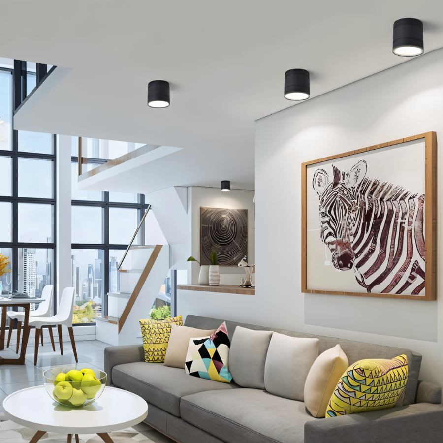 Clérachic black surface-mounted downlights spaced across the ceiling of an open-plan living room with a grey sofa and framed zebra print.