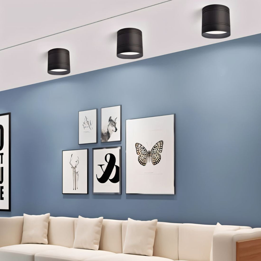Clérachic three black surface-mounted downlights above a blue wall with framed prints and a cream sofa below.