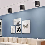 Clérachic three black surface-mounted downlights above a blue wall with framed prints and a cream sofa below.