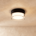 Clérachic compact round ceiling light with a black metal drum and a clear acrylic rim around a softly glowing centre.