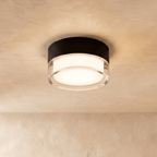 Clérachic compact round ceiling light with a black metal drum and a clear acrylic rim around a softly glowing centre.