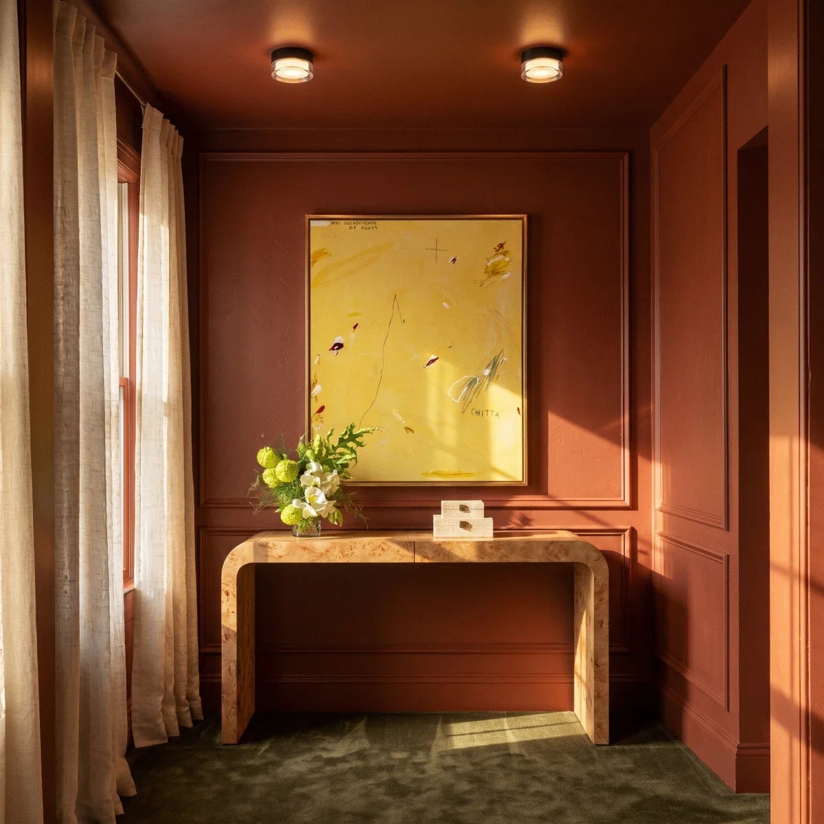 Pair of Clérachic round ceiling lights glowing above a burr-wood console and large yellow artwork in a terracotta-painted hallway.