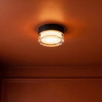 Clérachic black round ceiling light with a clear acrylic edge casting a warm amber glow across a terracotta-painted ceiling.