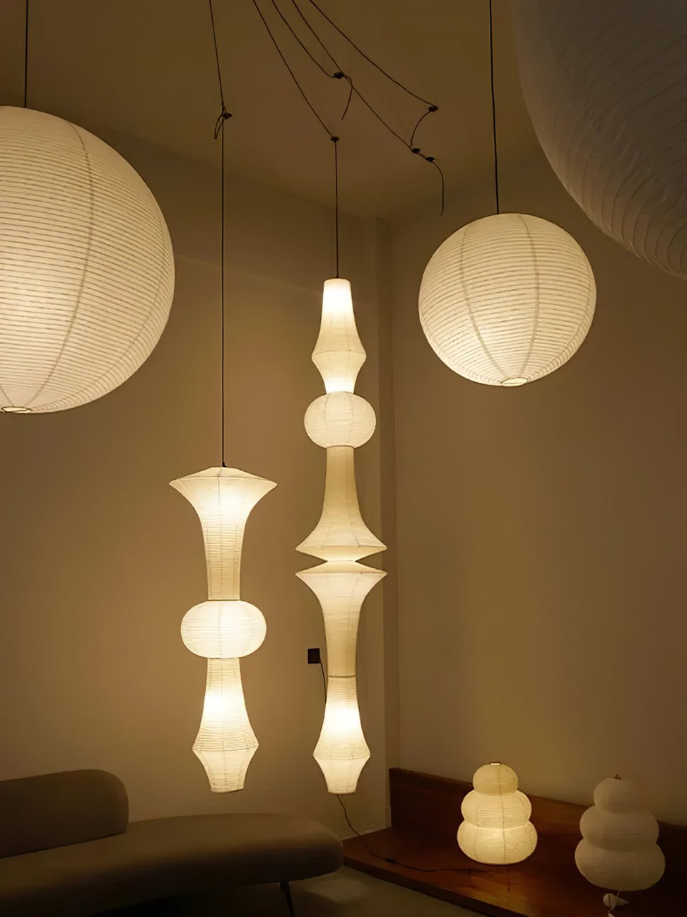 Clérachic washi paper pendant lit in a dark showroom corner beside a taller stacked drop, above a wood console holding two gourd-shaped table lamps.