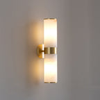 Clérachic Sway wall sconce in brushed brass, twin alabaster cylinders lit warm against a soft grey wall.