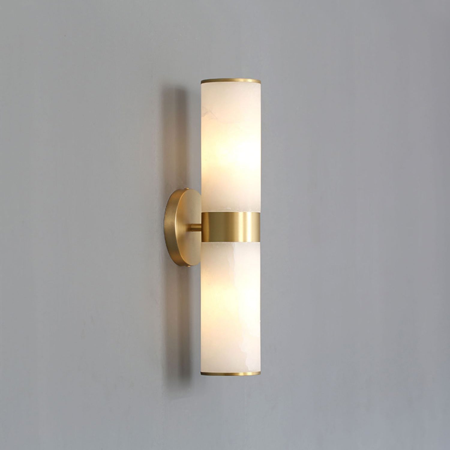 The Clérachic Sway unlit on a pale grey wall, showing the slim brass arm and matched stone cylinders.