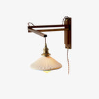 This Clérachic swing-arm wall light on a plain white backdrop, with a pleated white ceramic shade, brass fitting and a dark wood arm.
