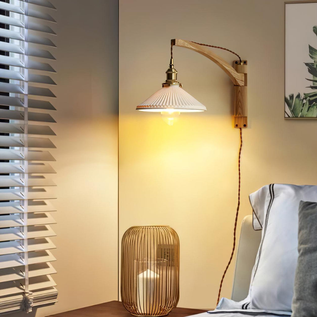 Warm light from a Clérachic wall light with a curved wood arm, beside a rattan lantern and a window blind in a bedroom corner.