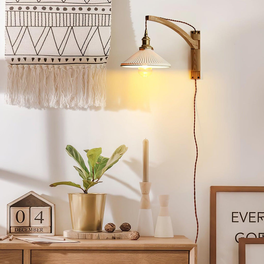 Beside a woven wall hanging, a Clérachic wall light with a curved wood arm and pleated shade hangs over a sideboard with a plant and a desk calendar.