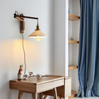 A Clérachic swing-arm wall light above a small wooden desk, with a blue curtain and open shelves in the corner of the room.