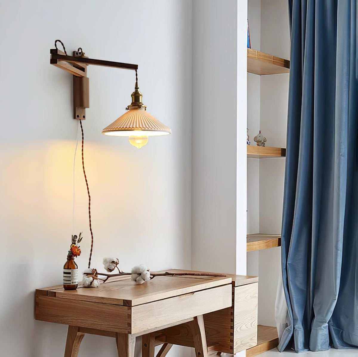 A Clérachic swing-arm wall light above a small wooden desk, with a blue curtain and open shelves in the corner of the room.